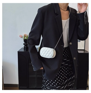 Close-up of white oval quilted chain bag with elegant diamond stitching on a young model