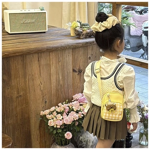 Detailed back view of a child wearing a yellow plaid crossbody bag with a bear charm
