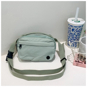 Close-up of a light green nylon crossbody bag for kids featuring a front zipper pocket