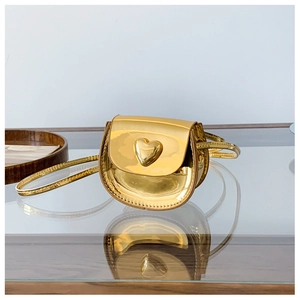 Detail of a shiny gold heart-shaped buckle on a patent leather mini crossbody bag
