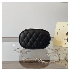 Detail of black quilted leather crossbody bag for kids with silver chain on glass surface