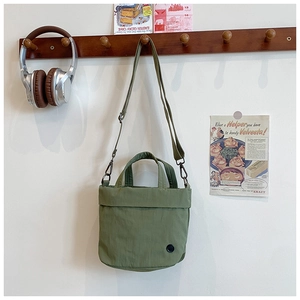 Olive green nylon child tote bag hanging on wooden wall hook with vintage background