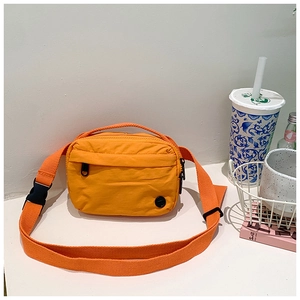 Close-up of vibrant orange crossbody bag with adjustable strap on white desk