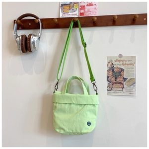 Detail of light green canvas crossbody bag featuring a round black logo on a wall hook