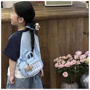 Close-up of light blue plaid kids handbag with cute brown bear charm and matching hair tie
