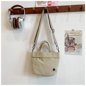 Detail of beige canvas kids crossbody bag with adjustable strap and top handle on wooden hook