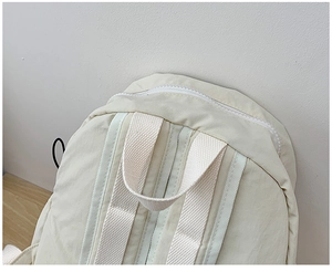 Top detail of cream school backpack showing sturdy handle, white zipper and nylon texture