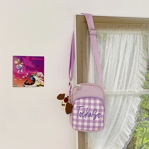 Detail of lavender plaid crossbody bag featuring a plush puppy charm and brand embroidery