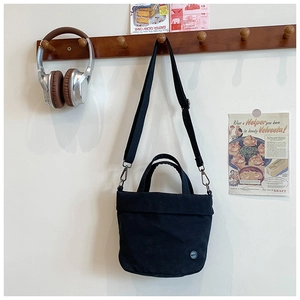 Detail of a black canvas crossbody bag with adjustable strap hanging on a wooden hook