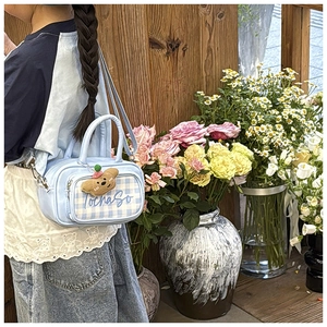 Detail view of a light blue plaid crossbody bag with a cute plush bear charm on a model