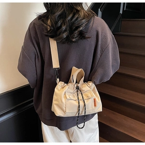 Détail du sac seau en toile beige clair avec fermeture à cordon et étiquette logo orange