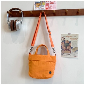 Close-up of bright orange canvas kids crossbody bag with adjustable strap on a hook