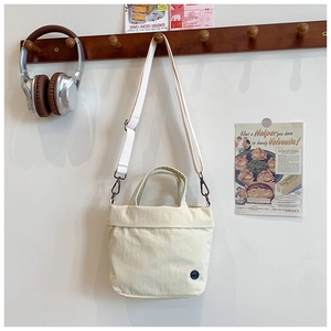 Detail of cream canvas messenger bag with round black logo and nylon shoulder strap