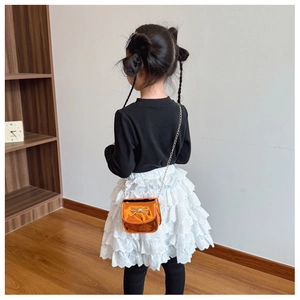 Détail du sac bandoulière orange métallisé avec nœud doré et chaîne élégante pour filles