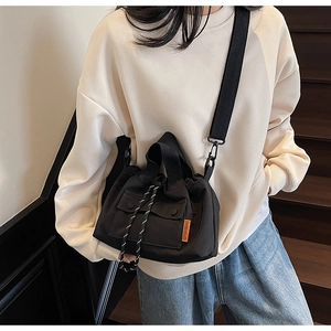 Détail du sac seau en toile noire avec étiquette orange et fermeture par cordon serrage