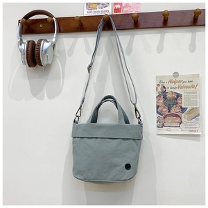 Detail of light blue canvas square bag with black badge and adjustable strap