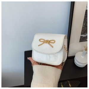 Détail d'un sac fille en cuir verni blanc avec nœud doré et bandoulière chaîne