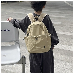 Detail of minimalist beige nylon school backpack showing the drawstring front pocket and zippers