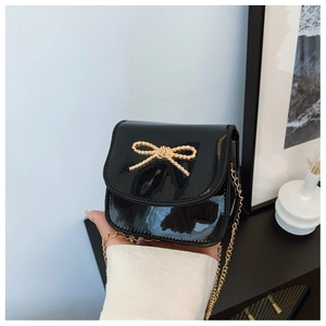 Détail d'un mini sac bandoulière enfant en cuir verni noir avec nœud doré et chaîne