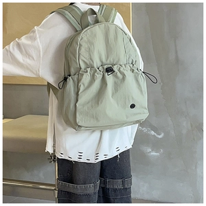 Detail of light green canvas backpack featuring a drawstring front pocket and round patch