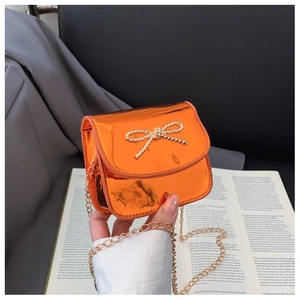 Détail du mini sac orange métallisé avec un nœud doré et une bandoulière chaîne