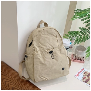 Detail of a beige minimalist school backpack with drawstring pocket in a lifestyle setting