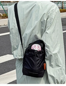 Détail du sac bandoulière léger en nylon noir avec cordon de serrage et étiquette orange