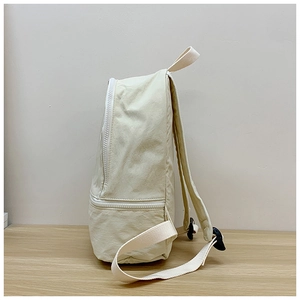 Detailed side view of the cream-colored nylon backpack featuring zipper and reinforced handle