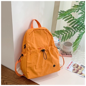 Detail of orange nylon school backpack showing the front drawstring pocket and texture