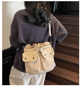 Detail of beige canvas bucket bag with multi-pockets and drawstring closure worn by model