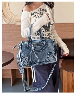 Detail of blue denim motorcycle shoulder bag with fringe and studs in a cafe setting