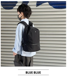 Street style shot of child wearing a minimalist black nylon backpack on a gray wall background