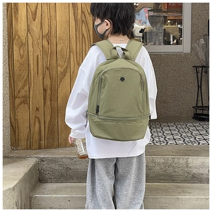 Olive green canvas kids backpack featuring a front zipper pocket in an outdoor setting