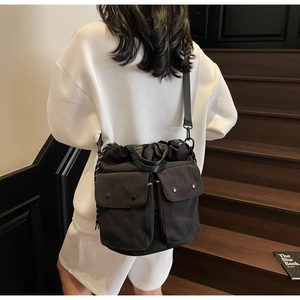 Detail of black drawstring bucket bag with dual front pockets worn by a model