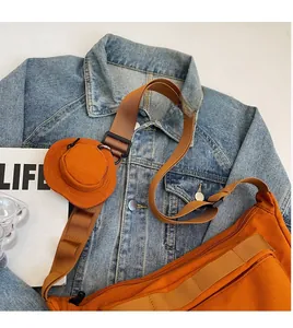 Détail d'un sac hobo en toile orange avec une large bandoulière et une mini pochette