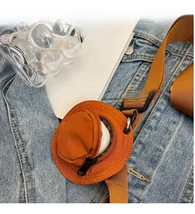 Gros plan d'une mini pochette ronde en nylon marron attachée à la sangle d'un sac en toile
