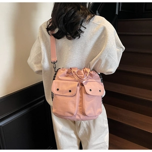 Pink nylon bucket bag shown on shoulder featuring dual front pockets and drawstring closure