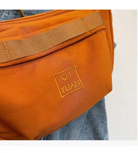Détail du sac à bandoulière en nylon orange montrant la texture tissée et le logo brodé