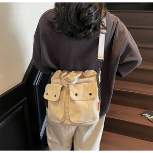 Detail view of beige canvas bucket bag featuring front flap pockets and wide shoulder strap