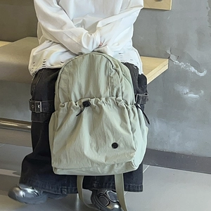 Green lightweight school backpack with drawstring closure shown in an outdoor lifestyle setting