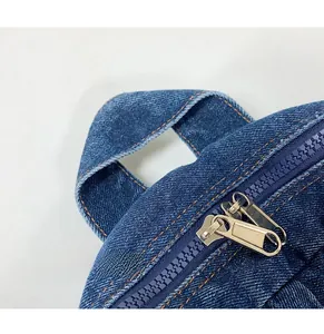 Detail of blue denim backpack with orange stitching and dual metal zippers