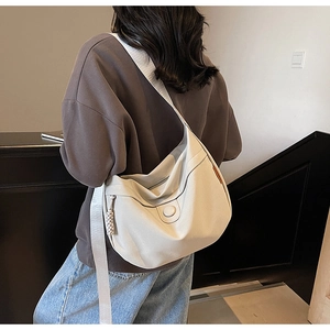 Detailed view of cream canvas hobo bag with wide strap and woven pendant on model