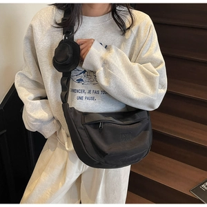 Détail du sac bandoulière croissant noir avec une petite pochette ronde sur la bandoulière
