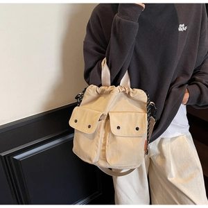 Detail of canvas drawstring bucket bag with dual front pockets and orange side label
