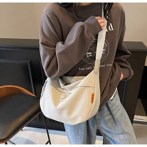 Close-up of beige canvas crescent bag with adjustable wide strap and side orange label