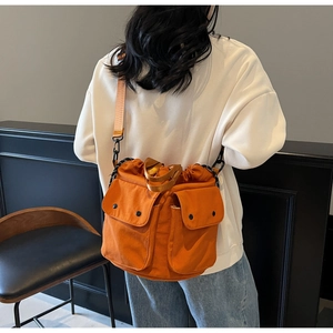Detail view of orange canvas bucket bag showing front pockets and adjustable strap