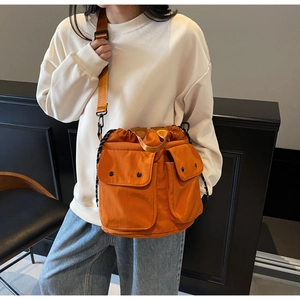 Close-up of orange drawstring bucket bag with utility pockets and wide nylon strap