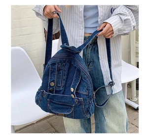 Detail of blue denim backpack with metal snaps and adjustable straps held by a model