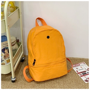 Detail view of orange minimalist kids backpack with zipper pockets on a woven rug