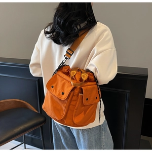 Detail of bright orange drawstring bucket bag with flap pockets and adjustable strap